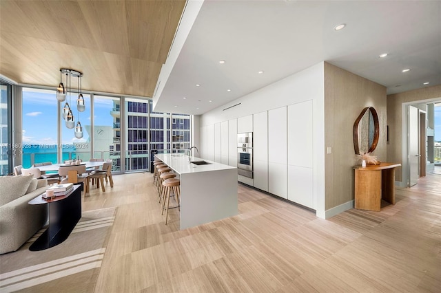 kitchen featuring white cabinets, hanging light fixtures, a kitchen island with sink, a wall of windows, and sink