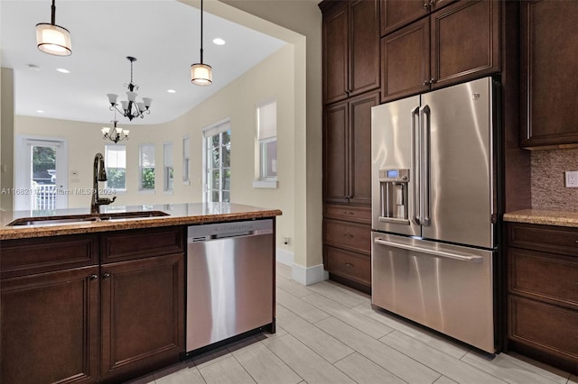 kitchen with hanging light fixtures, sink, appliances with stainless steel finishes, light stone counters, and a chandelier