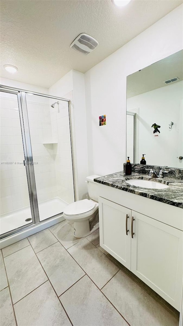 bathroom featuring a textured ceiling, walk in shower, toilet, vanity, and tile patterned floors