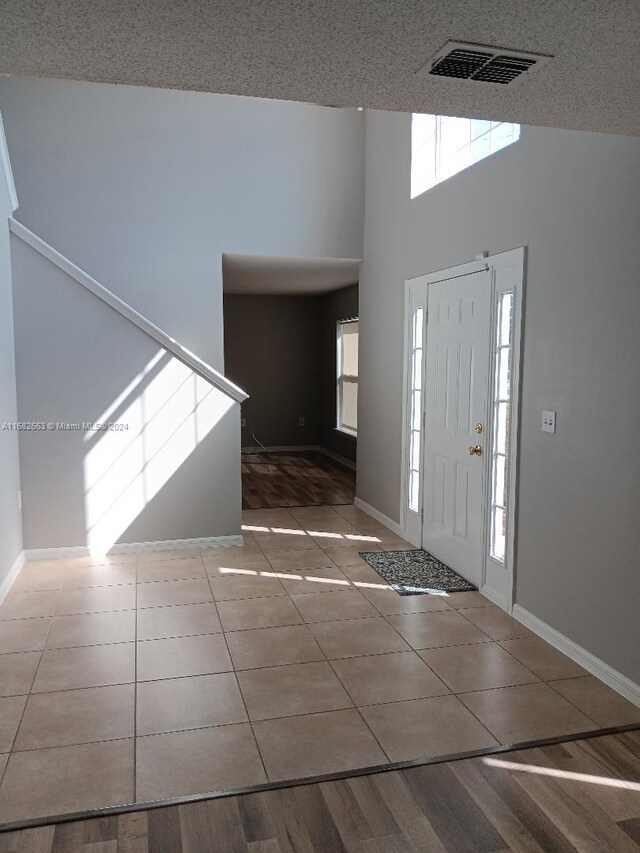 tiled entryway featuring visible vents, a high ceiling, and baseboards