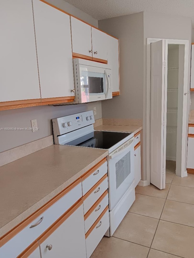 kitchen featuring white appliances, a textured ceiling, light tile patterned floors, and white cabinets