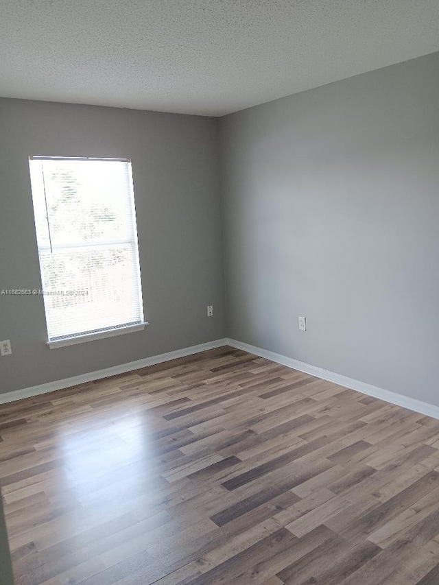 spare room featuring a textured ceiling, wood finished floors, and baseboards