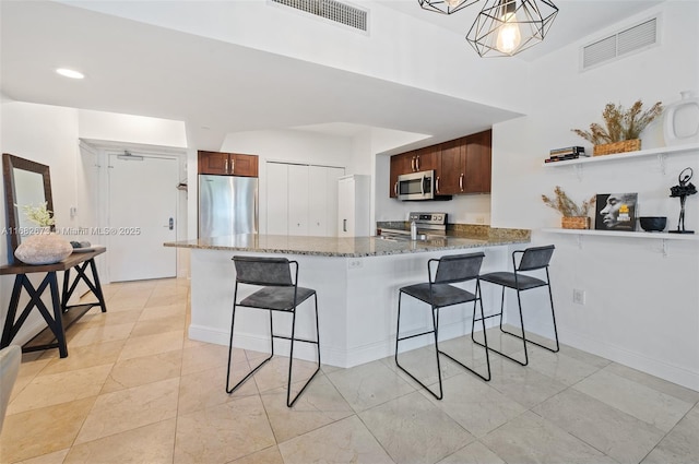 kitchen with appliances with stainless steel finishes, a breakfast bar, dark stone countertops, hanging light fixtures, and kitchen peninsula