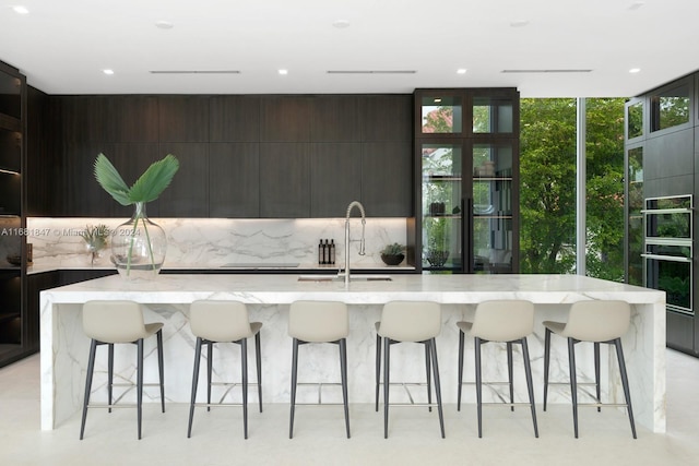 kitchen with a large island with sink, sink, decorative backsplash, and a kitchen bar