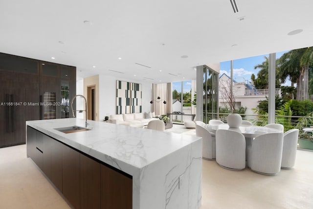 kitchen with a large island, sink, dark brown cabinetry, light stone counters, and floor to ceiling windows