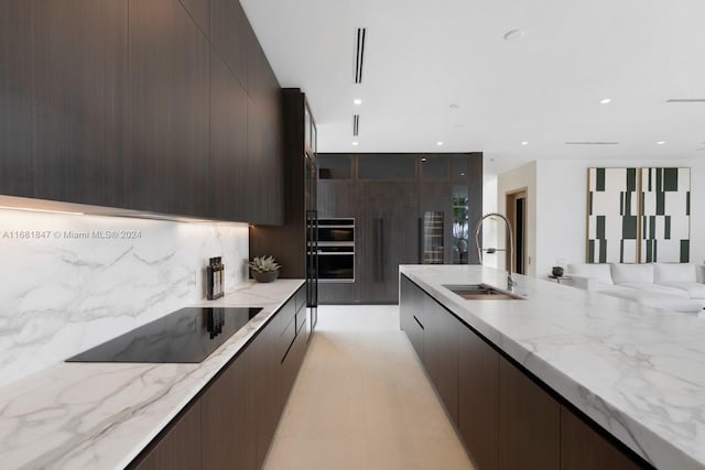 kitchen featuring backsplash, light stone countertops, black electric stovetop, dark brown cabinetry, and sink