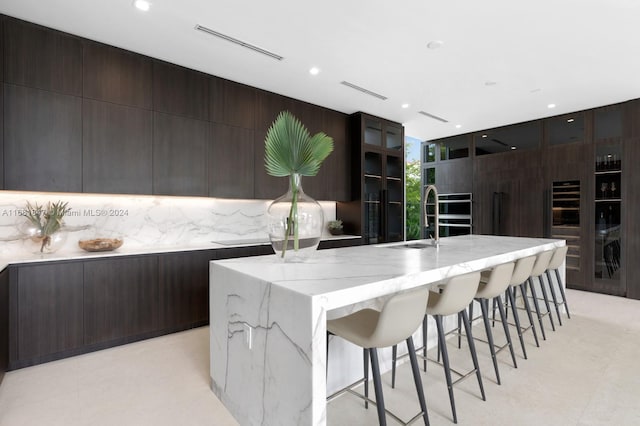 kitchen featuring decorative backsplash, a kitchen island with sink, sink, a breakfast bar, and light stone counters