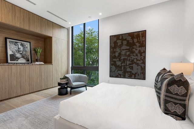 bedroom with wood walls, light wood-type flooring, and floor to ceiling windows