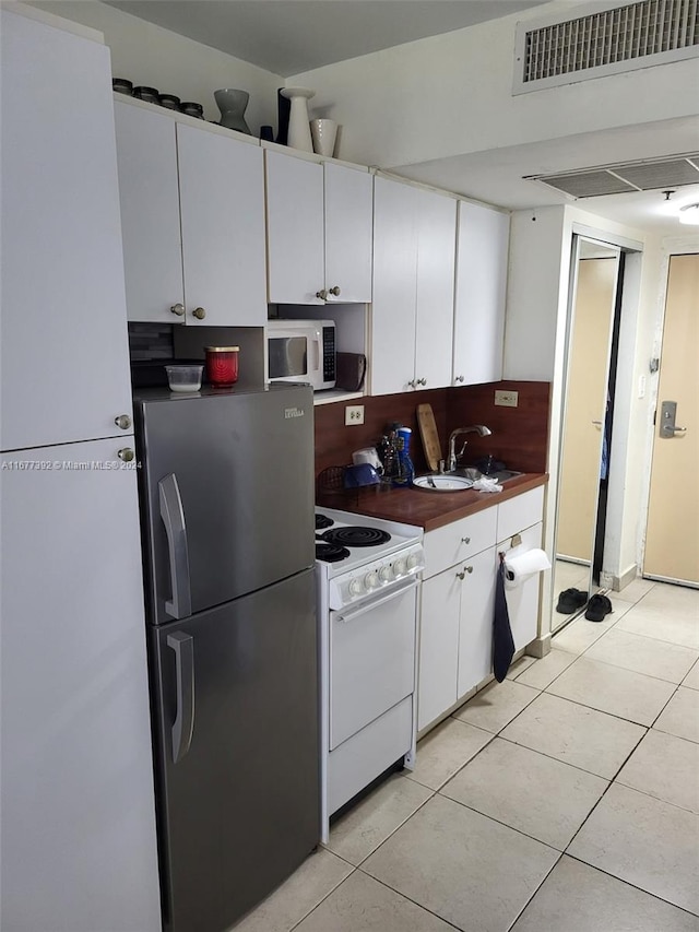 kitchen with white appliances, white cabinetry, light tile patterned floors, and sink