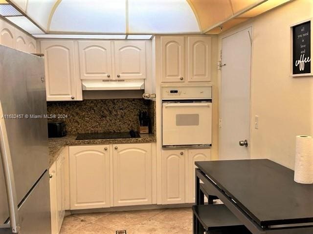 kitchen featuring stainless steel fridge, white oven, white cabinets, dark stone counters, and black electric stovetop