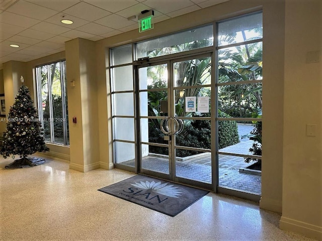doorway to outside featuring a drop ceiling, speckled floor, and baseboards