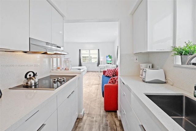 kitchen with backsplash, white cabinetry, hardwood / wood-style flooring, black electric stovetop, and ventilation hood