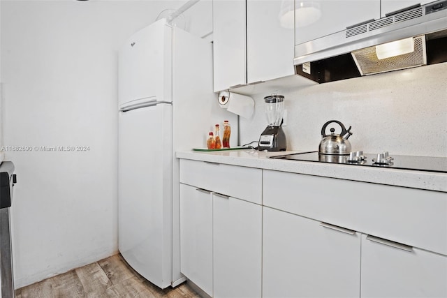 kitchen with white fridge, light wood-type flooring, white cabinetry, black stovetop, and range hood