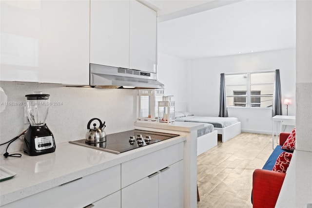 kitchen featuring light wood-type flooring, black electric cooktop, decorative backsplash, white cabinetry, and extractor fan