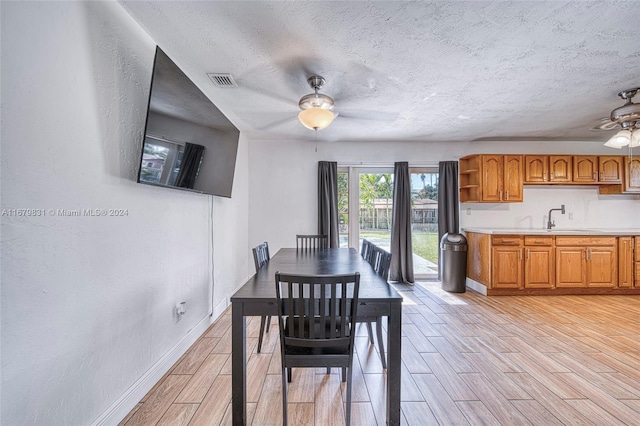 dining space with sink, light hardwood / wood-style flooring, a textured ceiling, and ceiling fan