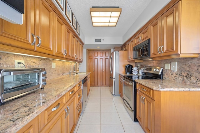 kitchen with sink, light tile patterned floors, appliances with stainless steel finishes, light stone counters, and tasteful backsplash