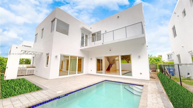 back of house with a balcony, exterior kitchen, a patio, and a fenced in pool