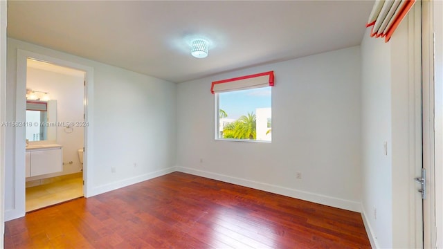 unfurnished bedroom featuring ensuite bathroom and hardwood / wood-style flooring