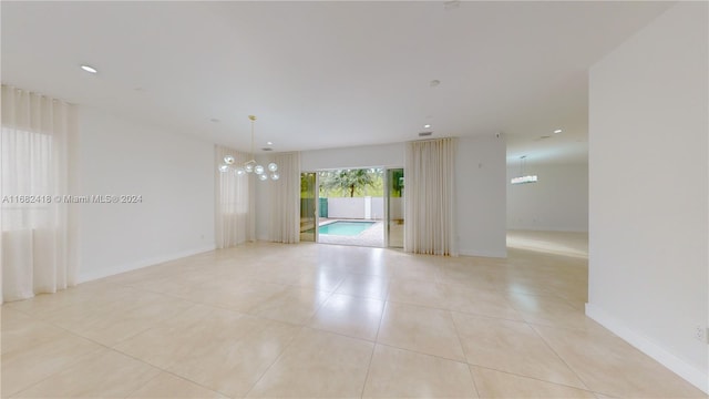 tiled spare room featuring an inviting chandelier