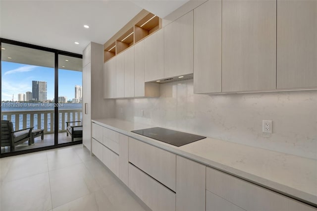 kitchen with black electric cooktop, range hood, a wall of windows, light stone counters, and tasteful backsplash