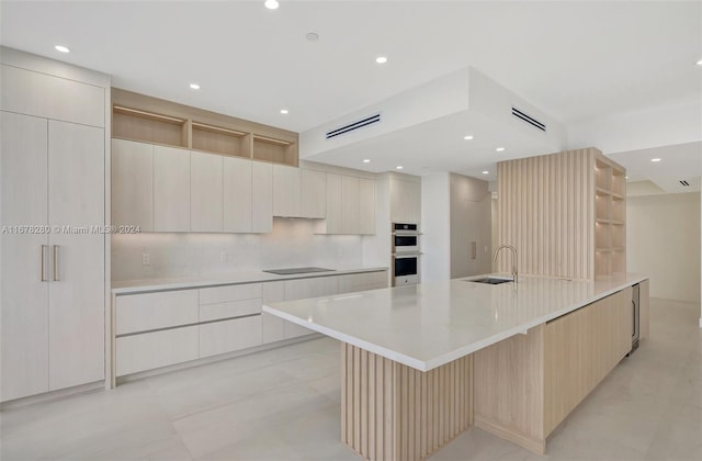 kitchen with backsplash, a large island with sink, black electric cooktop, sink, and stainless steel double oven