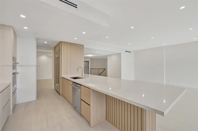 kitchen with a spacious island, light brown cabinets, stainless steel dishwasher, and sink