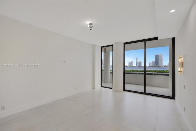 unfurnished room featuring a wall of windows, baseboards, tile patterned flooring, and a city view