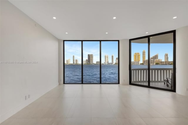 tiled empty room with a water view, a healthy amount of sunlight, and floor to ceiling windows