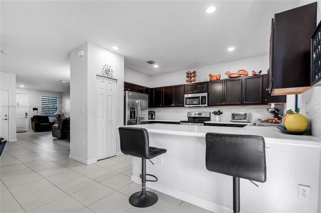 kitchen featuring kitchen peninsula, light tile patterned floors, stainless steel appliances, and a breakfast bar area