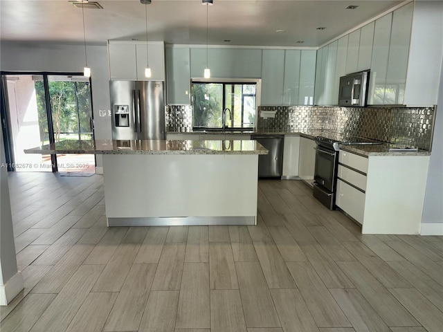 kitchen featuring stainless steel appliances, white cabinetry, dark stone countertops, and decorative light fixtures