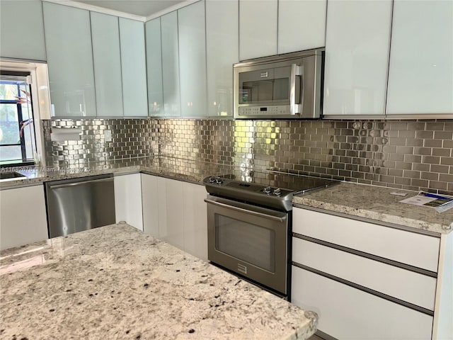 kitchen with stainless steel appliances, white cabinetry, light stone countertops, and backsplash