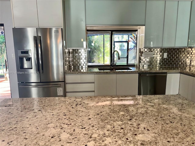 kitchen with green cabinets, stainless steel appliances, sink, and stone counters