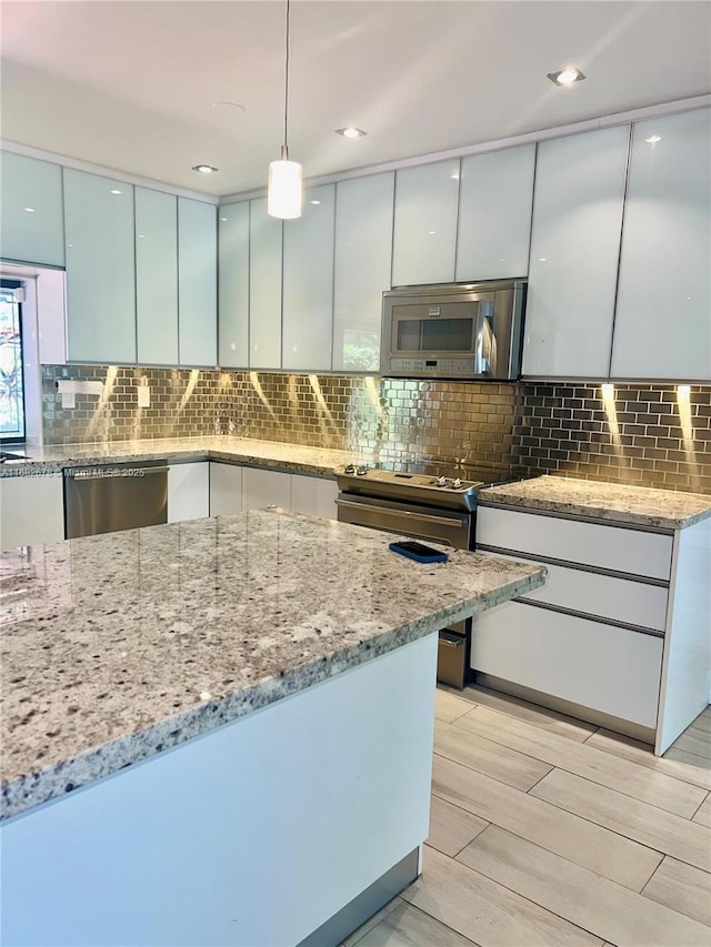 kitchen with hanging light fixtures, appliances with stainless steel finishes, backsplash, and light stone counters