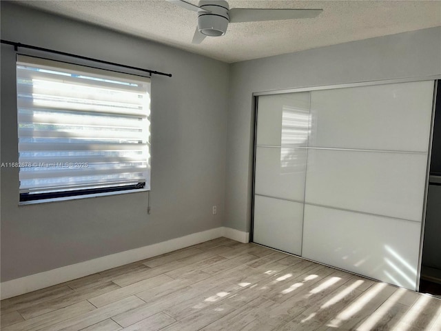 unfurnished bedroom with ceiling fan, a textured ceiling, a closet, and light wood-type flooring