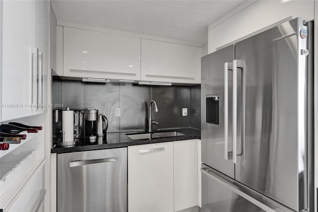 kitchen with appliances with stainless steel finishes, white cabinetry, sink, and backsplash