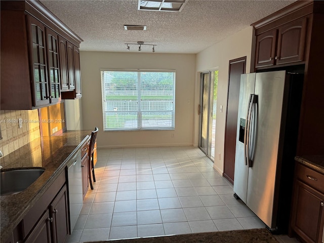 kitchen featuring decorative backsplash, stainless steel appliances, dark stone counters, and light tile patterned flooring