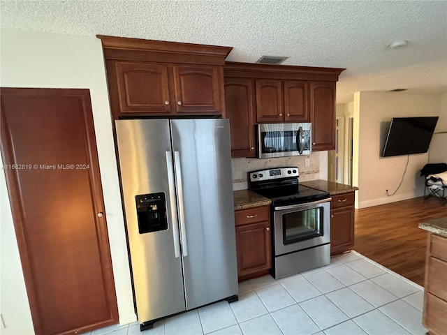 kitchen with dark stone countertops, a textured ceiling, decorative backsplash, appliances with stainless steel finishes, and light wood-type flooring