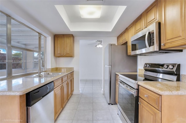 kitchen with stainless steel appliances, a tray ceiling, sink, light stone counters, and ceiling fan