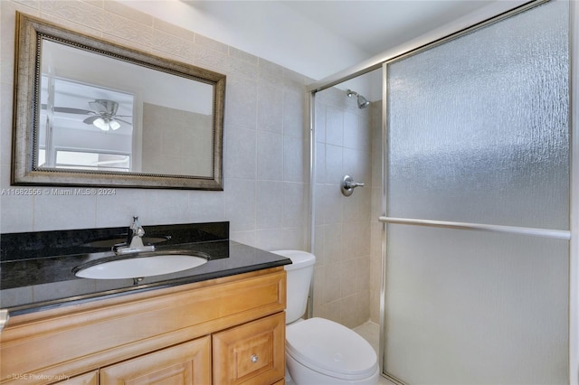 bathroom with toilet, vanity, walk in shower, tile walls, and ceiling fan