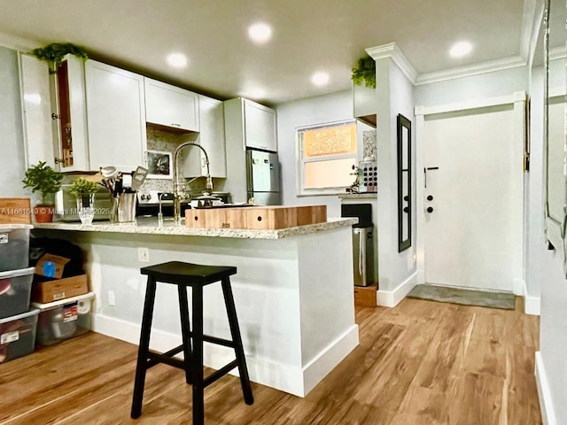 kitchen with white cabinetry, kitchen peninsula, stainless steel refrigerator, and light hardwood / wood-style flooring