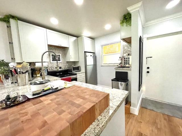 kitchen with white cabinets, crown molding, light wood-type flooring, light stone countertops, and stainless steel refrigerator