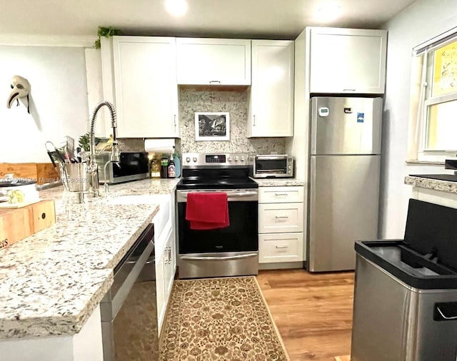 kitchen with white cabinets, light wood-type flooring, stainless steel appliances, and tasteful backsplash