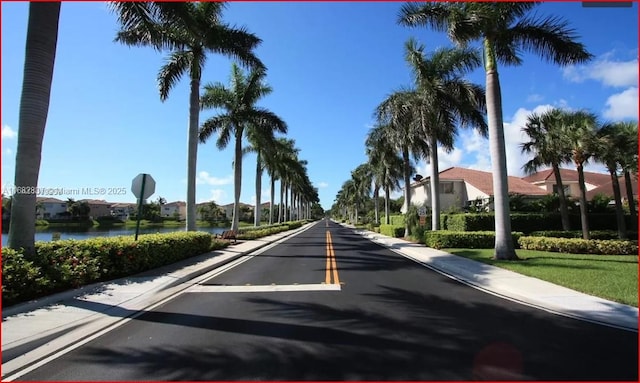 view of road with curbs, traffic signs, a water view, and sidewalks