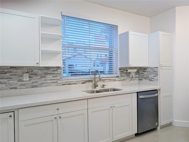 kitchen with light stone counters, decorative backsplash, white cabinetry, and a sink