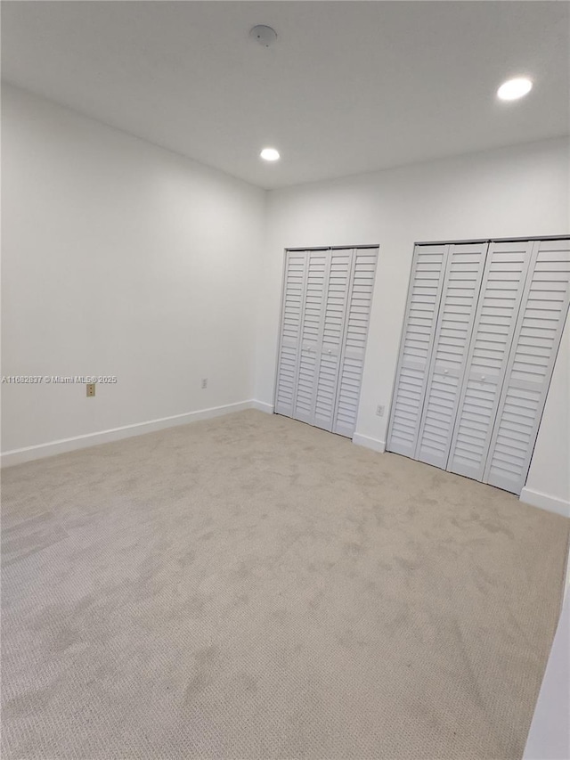 unfurnished bedroom with light carpet, recessed lighting, baseboards, and multiple closets