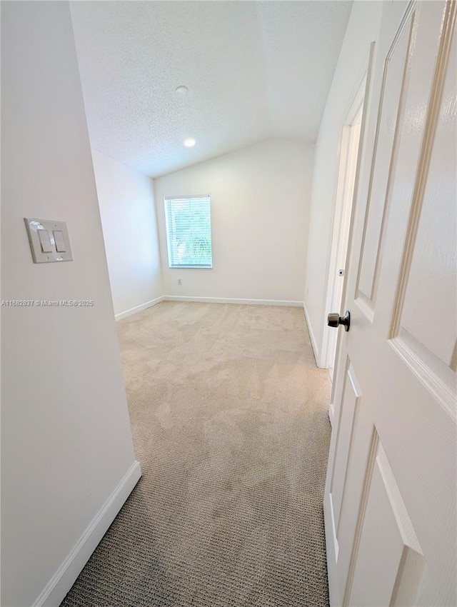 unfurnished room featuring light carpet, baseboards, a textured ceiling, and lofted ceiling