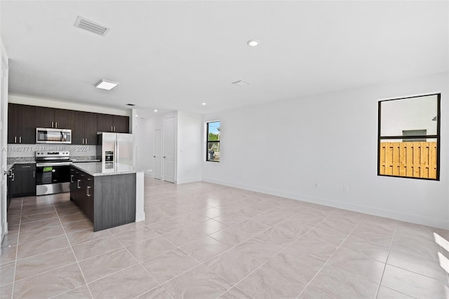 kitchen with backsplash, a kitchen island, light stone countertops, dark brown cabinetry, and stainless steel appliances