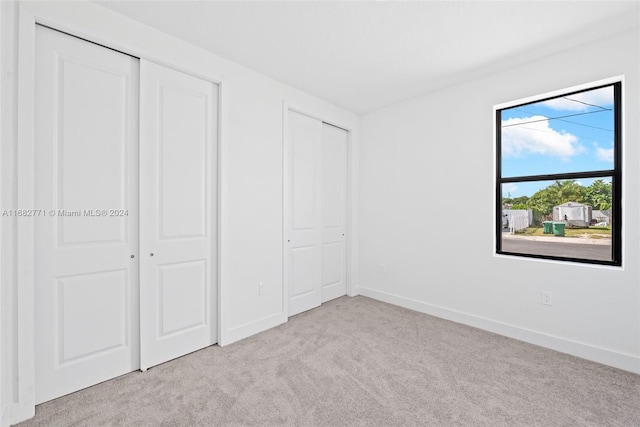 unfurnished bedroom with multiple closets and light colored carpet