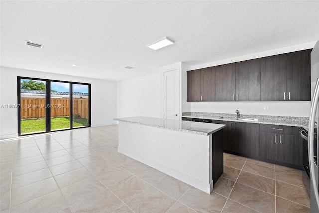 kitchen with light stone counters, light tile patterned floors, sink, dark brown cabinetry, and a center island