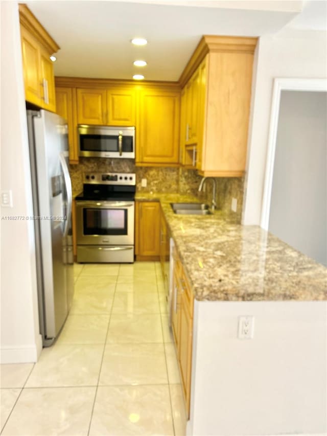 kitchen with light stone counters, light tile patterned floors, appliances with stainless steel finishes, backsplash, and sink